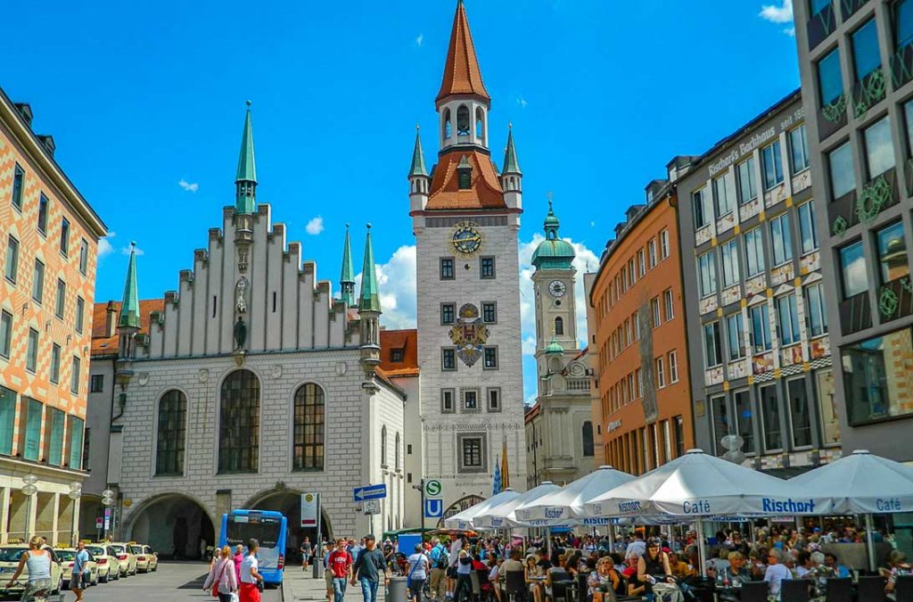 Pessoas lotam restaurantes nas calçadas em frente à Altes Rathaus, ou Prefeitura Antiga