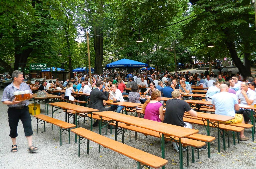 Homem carrega cervejas em meio às mesas comunitárias do biergarten Augustiner-Keller, em Munique