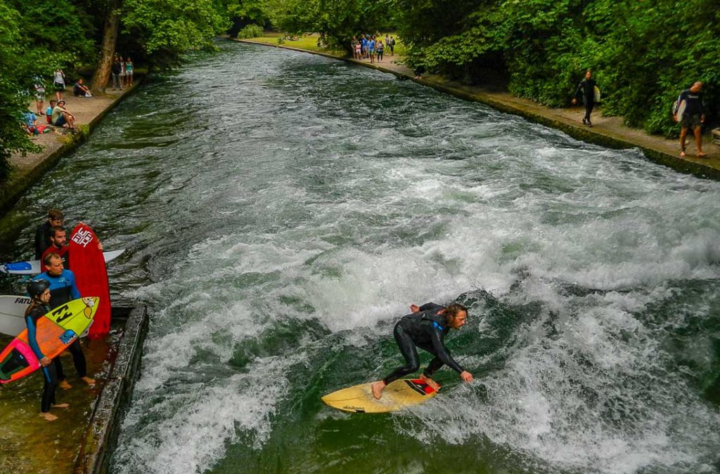 Homem surfa onda formada no Riacho Eisbach, dentro do Englischer Garten, em Munique