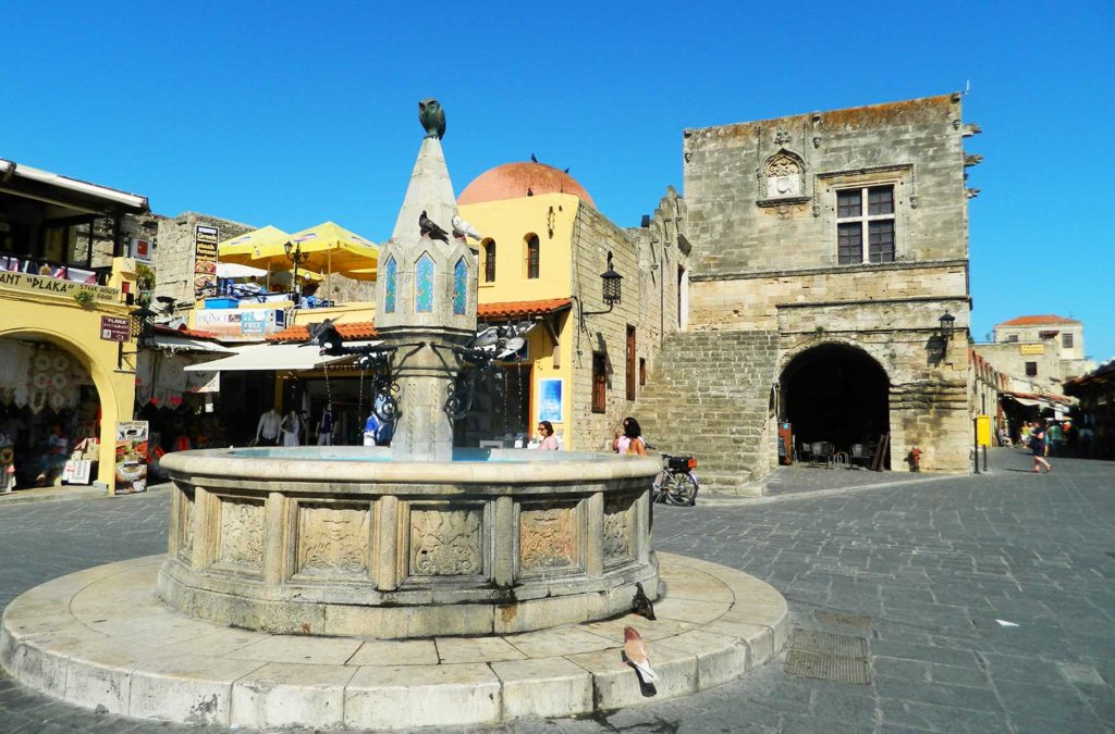 Pombas bebem água na fonte medieval da Praça de Hippocrates, em Rhodes