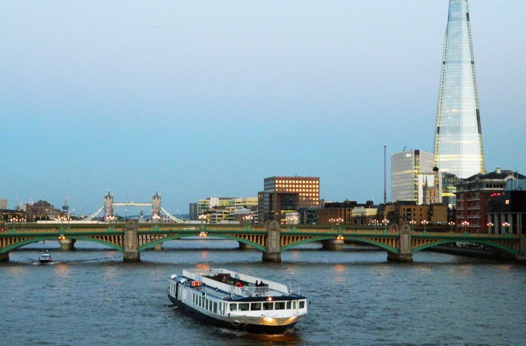 Barco navega pelo Rio Tâmisa ao anoitecer com o prédio The Shard ao fundo, em Londres