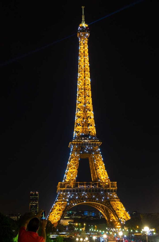 Pessoas fotografam a Torre Eiffel iluminada desde o Jardim do Trocadéro, em Paris