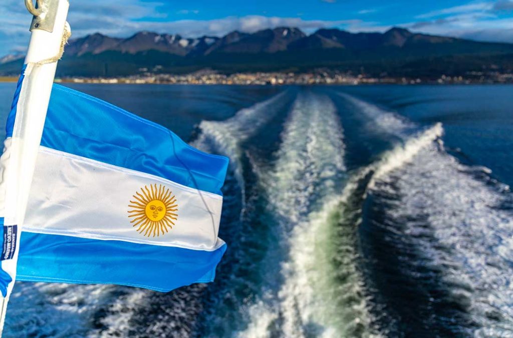 Bandeira argentina tremula em barco que leva turistas ao Canal de Beagle com a cidade de Ushuaia ao fundo