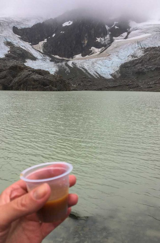 Mão segura copo de licor em frente ao Glaciar Vinciguerra, em Ushuaia