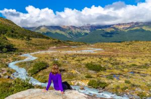 Mulher senta para admirar a vista na trilha da Laguna Esmeralda, em Ushuaia