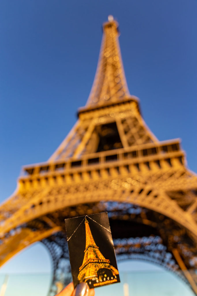 Mão segura ticket de entrada em frente à Torre Eiffel