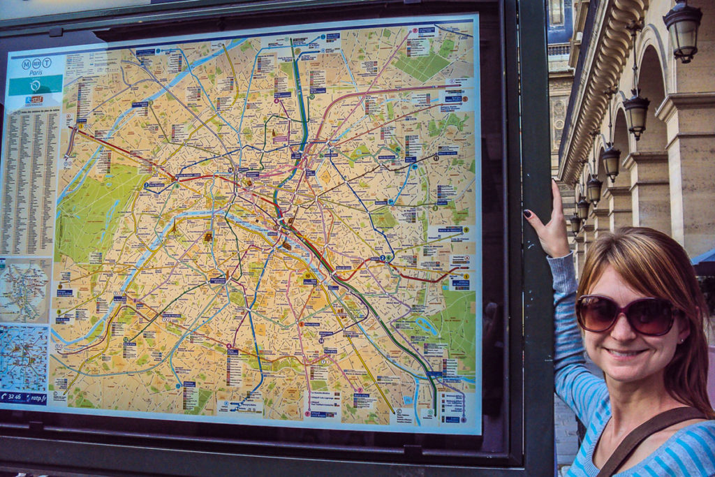 Mulher posa para foto ao lado do mapa do metrô de Paris