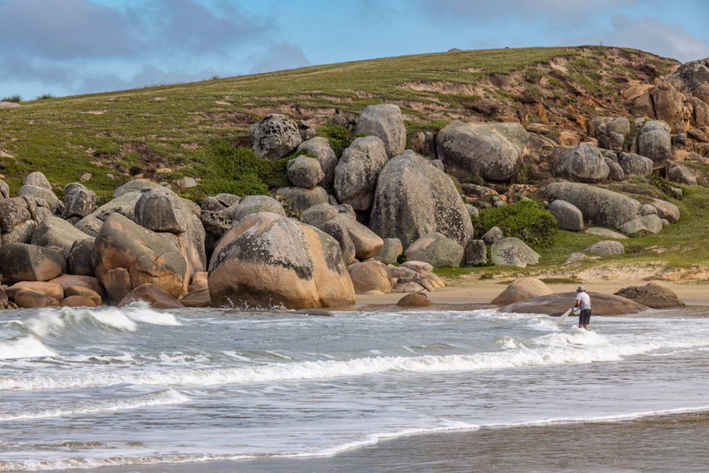 Homem joga rede de pesca na beira da Praia do Gravatá, em Laguna